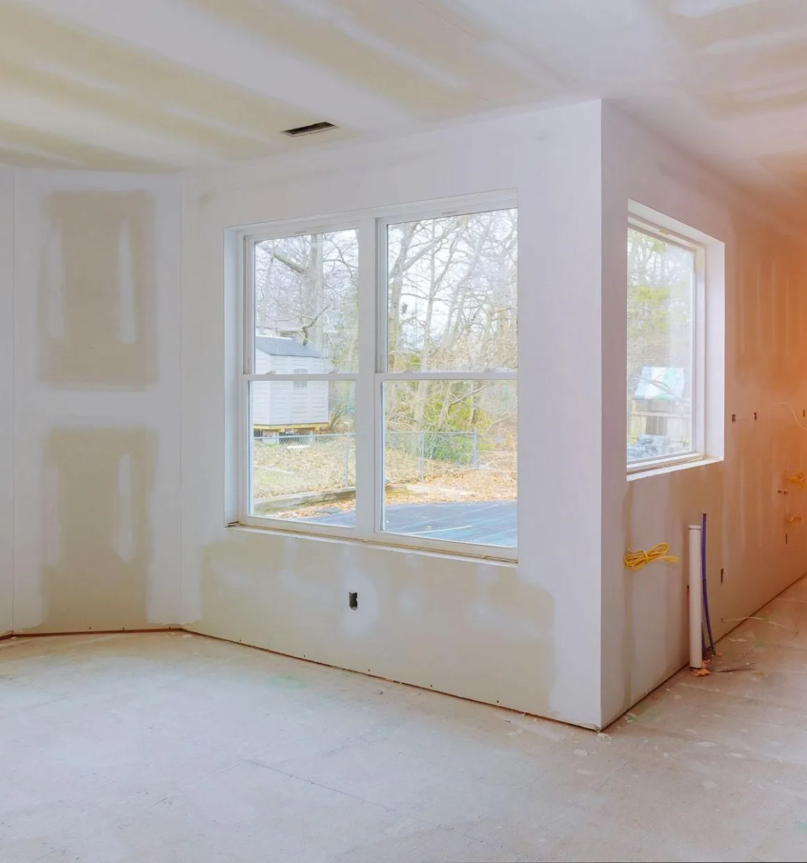 Freshly finished drywall in a modern home interior, showing clean taped seams, smooth compound lines, and natural daylight from large windows