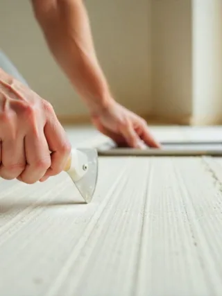 Close-up of hands finishing drywall with joint compound and knife in a clean, modern home