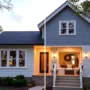 DIY home upgrades - Two-story house with light gray siding and a covered front porch, featuring a wreath and wicker furniture.