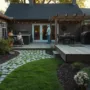 Backyard with a cobblestone pathway leading to a wooden deck patio, outdoor kitchen, barbecue grill, family gathering, sunny summer evening.
