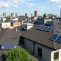 Rooftops in a modern city with solar panels and eco-friendly roofing repairs underway under a clear sky.